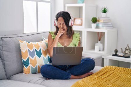 Foto de Mujer joven hispana usando laptop en casa sintiéndose mal y tosiendo como síntoma de resfriado o bronquitis. concepto de atención sanitaria. - Imagen libre de derechos