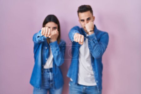 Téléchargez les photos : Jeune couple hispanique debout sur fond rose poing à coups de poing pour se battre, attaque agressive et en colère, menace et violence - en image libre de droit