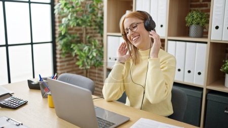 Téléchargez les photos : Jeune femme blonde femme d'affaires buvant du café écoutant de la musique au bureau - en image libre de droit