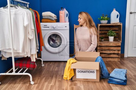 Photo for Hispanic woman putting clothes in donation box looking to side, relax profile pose with natural face with confident smile. - Royalty Free Image