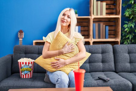 Photo for Caucasian woman eating popcorn watching a movie at home relaxed with serious expression on face. simple and natural looking at the camera. - Royalty Free Image
