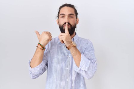 Téléchargez les photos : Homme hispanique à la barbe vêtu d'une chemise décontractée demandant à se taire avec le doigt sur les lèvres pointant la main sur le côté. silence et concept secret. - en image libre de droit