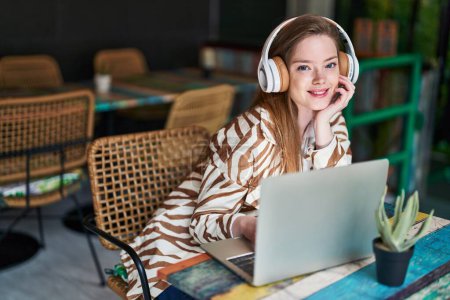 Téléchargez les photos : Jeune femme caucasienne utilisant ordinateur portable et écouteurs assis sur la table au restaurant - en image libre de droit