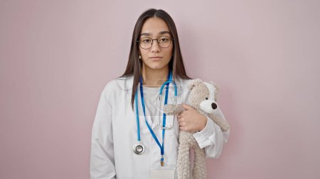 Photo for Young beautiful hispanic woman doctor holding teddy bear over isolated pink background - Royalty Free Image
