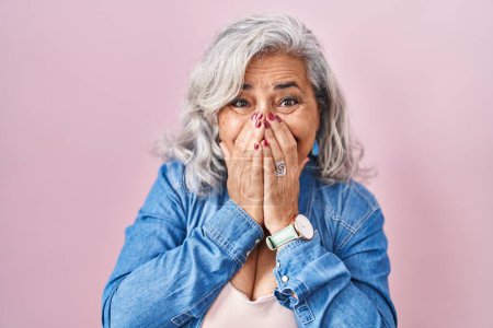 Photo for Middle age woman with grey hair standing over pink background laughing and embarrassed giggle covering mouth with hands, gossip and scandal concept - Royalty Free Image