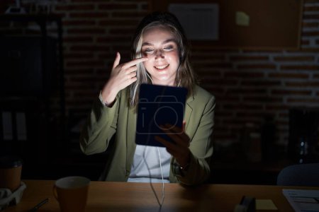 Photo for Blonde caucasian woman working at the office at night pointing with hand finger to face and nose, smiling cheerful. beauty concept - Royalty Free Image