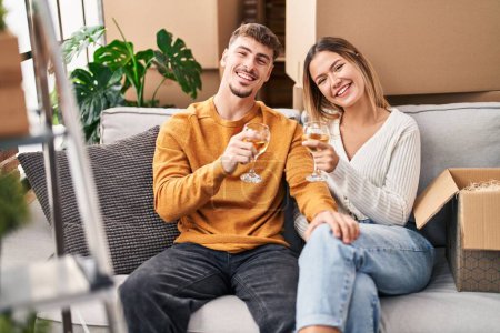 Photo for Young man and woman couple toasting with wine sitting on sofa at new home - Royalty Free Image