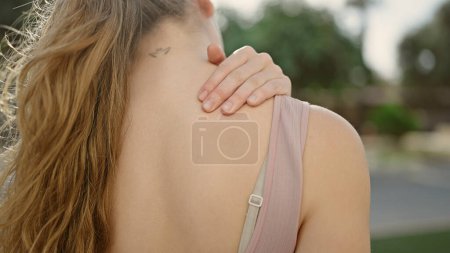 Foto de Mujer rubia joven con ropa deportiva que masajea la espalda para lesionarse en el parque - Imagen libre de derechos