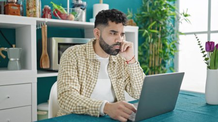 Photo for Young hispanic man using laptop with doubt expression at dinning room - Royalty Free Image