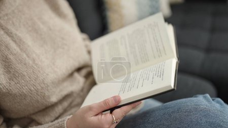 Photo for Young blonde woman reading book sitting on sofa at home - Royalty Free Image