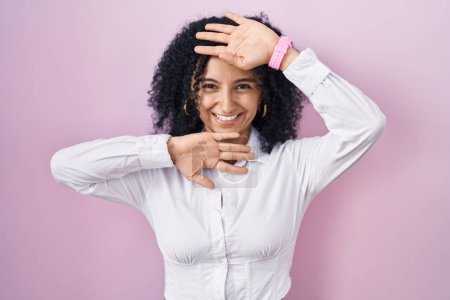 Foto de Mujer hispana con el pelo rizado de pie sobre fondo rosa sonriendo alegre jugando a echar un vistazo a un boo con las manos mostrando la cara. sorprendido y salido - Imagen libre de derechos