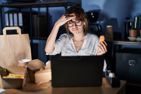 Photo for Young beautiful woman working using computer laptop and eating delivery food worried and stressed about a problem with hand on forehead, nervous and anxious for crisis - Royalty Free Image
