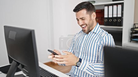 Téléchargez les photos : Jeune homme hispanique travailleur d'affaires en utilisant smartphone souriant au bureau - en image libre de droit