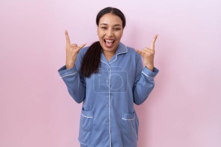 Photo for Young arab woman wearing blue pajama shouting with crazy expression doing rock symbol with hands up. music star. heavy music concept. - Royalty Free Image