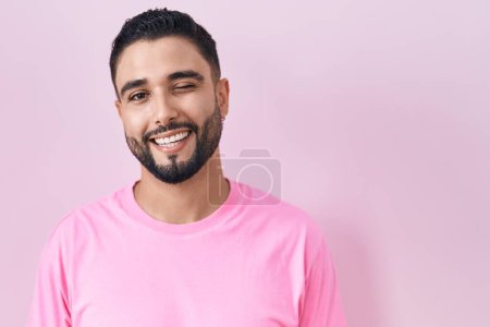 Photo for Hispanic young man standing over pink background winking looking at the camera with sexy expression, cheerful and happy face. - Royalty Free Image