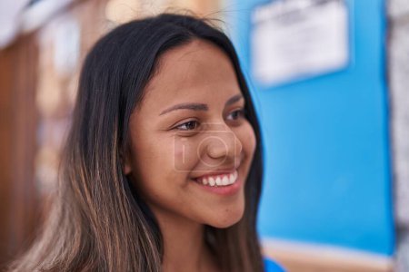 Téléchargez les photos : Jeune femme hispanique souriant confiant regardant vers le côté à la rue - en image libre de droit