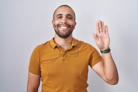Téléchargez les photos : Homme hispanique avec barbe debout sur fond blanc renonçant à dire bonjour heureux et souriant, geste de bienvenue amical - en image libre de droit