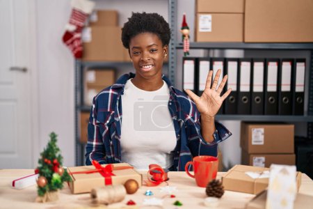 Photo for African american woman working at small business doing christmas decoration showing and pointing up with fingers number five while smiling confident and happy. - Royalty Free Image