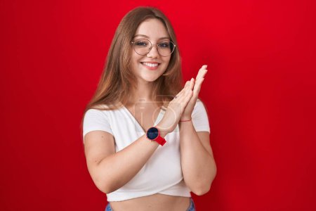 Téléchargez les photos : Jeune femme caucasienne debout sur fond rouge applaudissements et applaudissements heureux et joyeux, souriant mains fiers ensemble - en image libre de droit