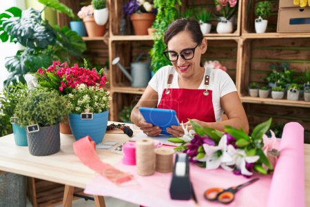 Téléchargez les photos : Young beautiful hispanic woman florist smiling confident using touchpad at flower shop - en image libre de droit