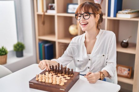 Téléchargez les photos : Jeune femme souriante confiante jouer aux échecs à la maison - en image libre de droit