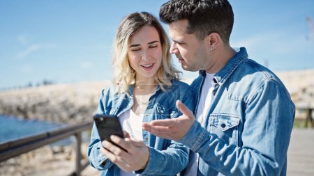 Téléchargez les photos : Couple homme et femme debout ensemble en utilisant un smartphone au bord de la mer - en image libre de droit
