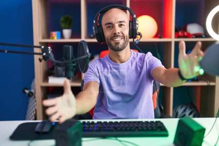 Photo for Middle age bald man playing video games wearing headphones looking at the camera smiling with open arms for hug. cheerful expression embracing happiness. - Royalty Free Image