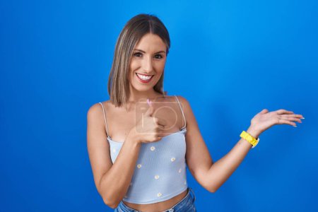 Photo for Young woman standing over blue background showing palm hand and doing ok gesture with thumbs up, smiling happy and cheerful - Royalty Free Image