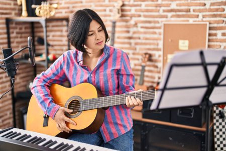 Foto de Young chinese woman musician playing guitar at music studio - Imagen libre de derechos