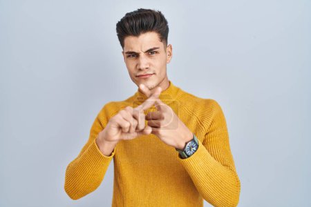 Photo for Young hispanic man standing over blue background rejection expression crossing fingers doing negative sign - Royalty Free Image