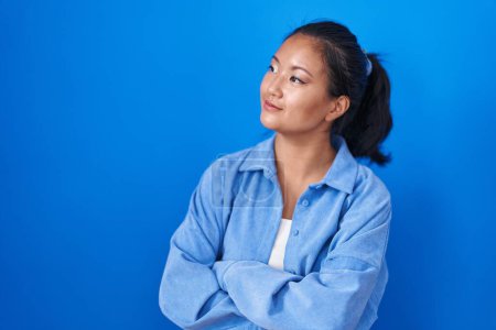Téléchargez les photos : Asiatique jeune femme debout sur fond bleu regardant sur le côté avec les bras croisés convaincu et confiant - en image libre de droit