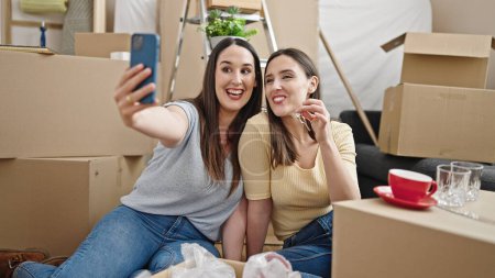 Foto de Dos mujeres hacen selfie por teléfono inteligente con llaves en el nuevo hogar - Imagen libre de derechos