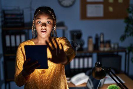 Téléchargez les photos : Femme afro-américaine avec des tresses travaillant au bureau la nuit avec une tablette faisant geste d'arrêt avec les mains paumes de main, expression de colère et de frustration - en image libre de droit