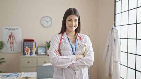 Photo for Young beautiful hispanic woman doctor smiling confident standing with arms crossed gesture at clinic - Royalty Free Image