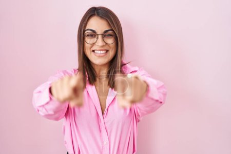 Téléchargez les photos : Jeune femme hispanique portant des lunettes debout sur fond rose pointant vers vous et la caméra avec les doigts, souriant positif et joyeux - en image libre de droit