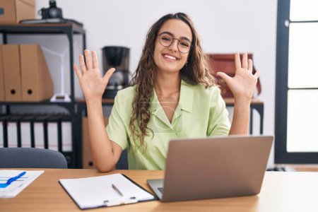 Photo for Young hispanic woman working at the office wearing glasses showing and pointing up with fingers number ten while smiling confident and happy. - Royalty Free Image