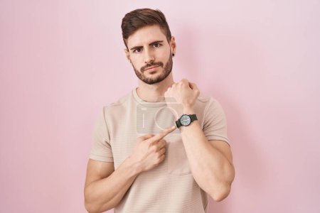 Téléchargez les photos : Homme hispanique avec barbe debout sur fond rose à la hâte pointant vers regarder le temps, l'impatience, regardant la caméra avec une expression détendue - en image libre de droit