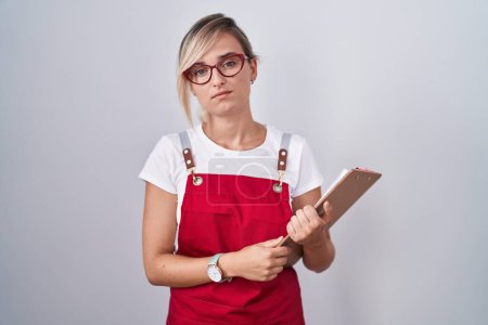 Photo for Young blonde woman wearing waiter uniform holding clipboard looking sleepy and tired, exhausted for fatigue and hangover, lazy eyes in the morning. - Royalty Free Image