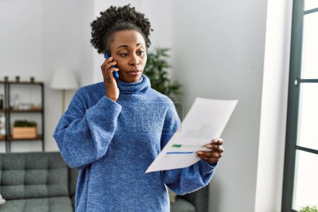 Foto de Mujer afroamericana hablando en factura de lectura de teléfonos inteligentes en casa - Imagen libre de derechos