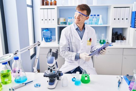 Photo for Young man scientist smiling confident reading report at laboratory - Royalty Free Image