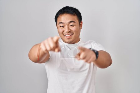 Foto de Joven hombre chino de pie sobre fondo blanco apuntando a usted y la cámara con los dedos, sonriendo positivo y alegre - Imagen libre de derechos