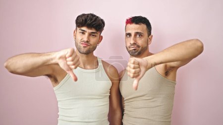 Téléchargez les photos : Deux hommes couple faisant signe négatif avec pouce vers le bas sur fond rose isolé - en image libre de droit