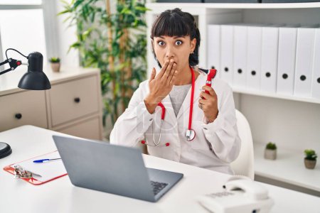 Photo for Young hispanic doctor woman holding ear thermometer covering mouth with hand, shocked and afraid for mistake. surprised expression - Royalty Free Image