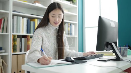 Téléchargez les photos : Jeune étudiante chinoise utilisant l'écriture informatique sur ordinateur portable à l'université de la bibliothèque - en image libre de droit