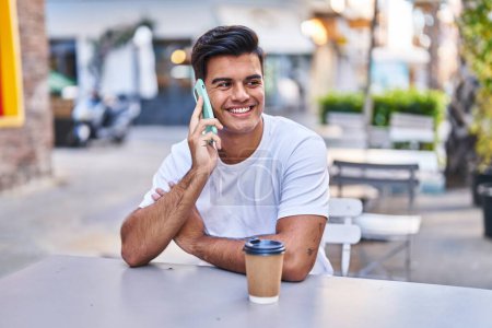 Téléchargez les photos : Jeune homme hispanique parlant sur smartphone boire du café à la terrasse du café - en image libre de droit