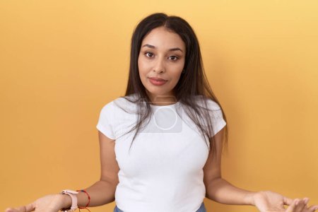 Photo for Young arab woman wearing casual white t shirt over yellow background clueless and confused with open arms, no idea concept. - Royalty Free Image