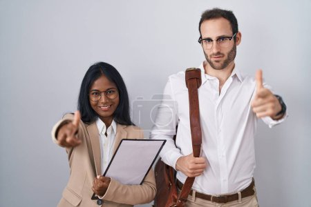 Téléchargez les photos : Couple d'affaires interracial portant des lunettes pointant du doigt la caméra avec un visage heureux et drôle. bonne énergie et vibes. - en image libre de droit