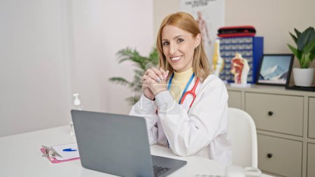 Téléchargez les photos : Jeune femme blonde médecin utilisant un ordinateur portable travaillant à la clinique - en image libre de droit