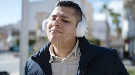 Téléchargez les photos : Jeune homme hispanique écoutant de la musique et dansant dans la rue - en image libre de droit