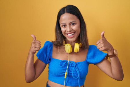Photo for Hispanic young woman standing over yellow background success sign doing positive gesture with hand, thumbs up smiling and happy. cheerful expression and winner gesture. - Royalty Free Image